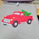 Faux Yarn Red Christmas Truck DTF Heat Transfer, embroidered holiday-themed red truck with green Christmas tree in bed, including decorative holly, on a grey fabric background.