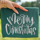 Merry Christmas Faux Metallic Silver DTF Heat Transfer, a person holding a green gift box with a silver metallic 'Merry Christmas' design on it.