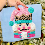 Faux Yarn Leopard Nutcracker DTF Heat Transfer, colorful plush velvet textured image of a Nutcracker with a pink hat, turquoise accents, leopard pattern, and a white beard on a blue background.