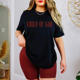 Child Of God RED DTF Heat Transfer, a woman wearing a black t-shirt with red text and red shorts, standing indoors with decorative plants and a mirror in the background.