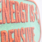 My Energy Is Expensive PUFF Embroidered HAT/POCKET Patch, close-up view showing textured orange embroidery on a mint green fabric background.