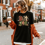 Faux Yarn But God Fall DTF Heat Transfer, a woman wearing a black T-shirt with fall-themed embroidered words and designs, holding a coffee cup outdoors.