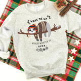 Wake Me When Winter Is Over Sloth Screen Print Heat Transfer, humorous winter-themed sweatshirt with a cute sloth wearing a winter hat and scarf, hanging on a tree branch surrounded by snowflakes.
