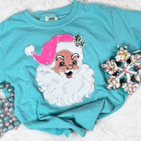 Youth Pink Santa Sequin Patch, festive pink Santa Claus face embroidered on a turquoise T-shirt with holiday decorations around.