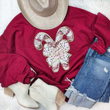 Pink & White Candy Cane Bow Sequin Patch, close-up view of a decorative patch featuring sequined candy canes and a bow on a red sweatshirt, accompanied by a beige hat, ripped jeans, and white ankle boots.