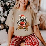 Faux Yarn Festive Raccoon DTF Heat Transfer, Christmas-themed raccoon wearing Santa hat and riding reindeer on beige t-shirt.