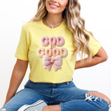 Faux Fluffy God Is Good DTF Heat Transfer, a pink fluffy textured design with the words 'GOD is GOOD' and a bow on a woman's yellow t-shirt.