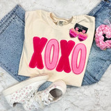 XOXO Fluffy Chenille Patch, cream-colored T-shirt with pink and red chenille patches spelling XOXO, paired with light blue denim jeans and white floral print sneakers.