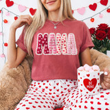 Faux Lace Mama Valentine Patchwork DTF Heat Transfer, woman wearing a pink t-shirt with heart patterned lettering spelling 'MAMA' and holding a Valentine's themed mug filled with pink marshmallows.