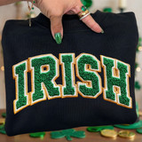 Faux Chenille Irish DTF Heat Transfer, close-up of green and gold embroidered word 'Ireland' on black sweatshirt.