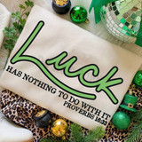 Luck Has Nothing To Do With It DTF Heat Transfer, embroidered design on a fabric with green and black text and a playful font, surrounded by holiday decorations including green ornaments, a mirrored disco ball, and festive greenery.