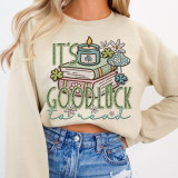 It's Good Luck To Read DTF Heat Transfer, colorful embroidered design on a beige sweatshirt featuring books, flowers, a candle, and decorative text.