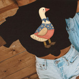 Faux Patchwork Goose DTF Heat Transfer, a fabric patchwork design of a goose with a blue bow tie, floral blue and beige patterns, and patchwork details on a person's black t-shirt.