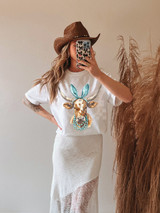 Western Easter Cow DTF Heat Transfer, colorful cow with bunny ears and pearl necklace design on a white T-shirt worn by a woman with a cowboy hat.