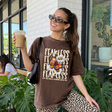Fearless Butterfly DTF Heat Transfer, woman wearing a brown t-shirt with butterfly and flower design, holding iced coffee, outdoor cafe scene.