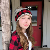 C.C. Buffalo Plaid Beanie, woman wearing a wool knit buffalo plaid beanie with mixed colors including red, black, and white, featuring a pom-pom on top.