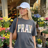 Faux Fabric Patchwork Pray DTF Heat Transfer, woman wearing a dark gray T-shirt with 'PRAY' text and a white baseball cap, standing in a flower shop with colorful spring flowers.