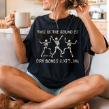 Dry Bones Rattling DTF Heat Transfer, graphic T-shirt with dancing skeletons and text, casual woman holding cup in a cozy home setting