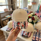 Patriotic Floral Cotton Blank Hat, beige cap with a floral print brim featuring red, white, and black colors, displayed on a person's hand in a store setting.