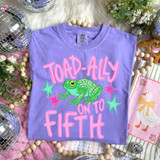 Toad-Ally On To Pink DTF Heat Transfer, colorful graphic T-shirt with green toad and pink text, on lavender fabric surrounded by decorative items.