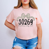 Peachtree City, GA Zip Code Bow DTF Heat Transfer, pink t-shirt with a bow graphic and the zip code 30269 and city name printed on it.
