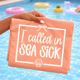 Product I Called In Sea Sick WHITE DTF Heat Transfer, white text design on peach-colored fabric with a bow and shell graphic, pool with floaties in the background.