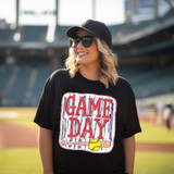 Game Day Softball DTF Heat Transfer, a vibrant and colorful design featuring the text 'Game Day' with a softball and bat illustration, on a black t-shirt worn by a smiling woman at a stadium.