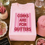 Pink “Corks Are For Quitters” puff screen print transfer on a pastel pink t-shirt with raised textured lettering and retro pink stripe background.