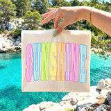 Sunshine Rainbow Seersucker DTF Heat Transfer, colorful rainbow striped text on white fabric, outdoor scenic background with water and rocks.