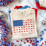 Paws & Stripes Forever DTF Heat Transfer, patriotic American flag design with paw prints and dog silhouettes on a cream-colored t-shirt surrounded by red, white, and blue decorations.