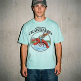 Who's Your Crawdaddy DTF Heat Transfer, a graphic on a light blue T-shirt featuring a person riding a large red crawfish in water with the text 'who's your CRAWDADDY' above.