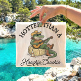 Hotter Than A Hoochie Coochie Gator DTF Heat Transfer, a colorful design featuring an alligator wearing sunglasses, a cowboy hat, and boots, playing guitar and sitting on hay, with a bottle of alcohol nearby and the text 'Hootter Than A Hoochie Coochie' on a fabric background.
