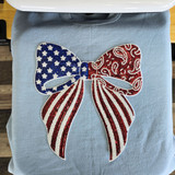 Close-up of oversized patriotic sequin bow patch with blue star print, red paisley detailing, and rhinestone embellishments heat pressed onto a light blue sweatshirt.