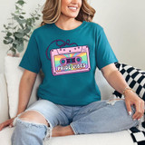 Pride Vibes Cassette DTF Heat Transfer, colorful cassette tape design with rainbow background and 'Pride Vibes' text on a teal T-shirt worn by a smiling woman.