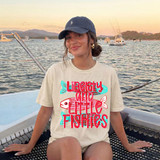 Liberty and Little Fishies DTF Heat Transfer, colorful graphic design with fish and butterflies on a woman's t-shirt with a seaside background at sunset.