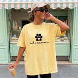 Dog Whisperer BLACK DTF Heat Transfer, product image of a yellow T-shirt with a black paw print and the word 'whisper' written below, worn by a smiling woman outdoors.