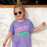 Later Gator DTF Heat Transfer, a colorful cartoon alligator and the word 'LATER' on a purple t-shirt worn by a little girl.
