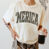 Merica Camo DTF Heat Transfer, image shows a person wearing a cream-colored T-shirt with a camo-style 'MERICA' text in bold letters.
