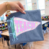 Teach Pennant DTF Heat Transfer, colorful educational fabric banner with the word Teach in pink and purple letters, applied on a blue cloth in a classroom setting.