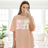 Senior 2027 Coquette DTF Heat Transfer, colorful and decorative design on a light pink T-shirt.