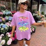 Bass Trio DTF Heat Transfer, vibrant colorful fish graphic on light purple T-shirt worn by a smiling woman in a flower shop