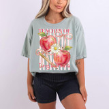 Teacher Of Tiny Humans DTF Heat Transfer, colorful design featuring apples, daisies, and a pencil on a light gray T-shirt worn by a woman.