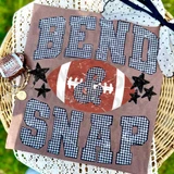 Bend And Snap Football DTF Heat Transfer, football themed fabric design with checkered pattern letters and football graphic on a brown background, placed on a pink cloth with stars and jewelry.