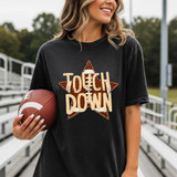 Touchdown Football Star DTF Heat Transfer, a woman wearing a black T-shirt with a football-themed design and the text 'Touch Down' on the front, holding an American football on an outdoor football field.