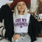 Distressed Oh My Gourdness PLUM DTF Heat Transfer, woman wearing a white t-shirt with purple text and a pumpkin graphic, smiling with a cowboy hat and casual outfit.