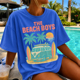 Vintage Coastal Surf Bus DTF Heat Transfer, graphic T-shirt with beach scene featuring palm trees, a sunset, surfboards, and a vintage van on a summer day by the pool.