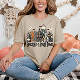 Spooky In A Small Town DTF Heat Transfer, a woman wearing a beige T-shirt with a Halloween-themed haunted house graphic and the phrase "Spooky in a Small Town."