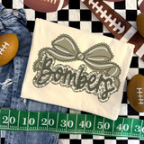 Camo Bow School Mascot DTF Heat Transfer, camouflage bow design with the word 'Bombers' in cursive, printed on a fabric piece, surrounded by footballs, denim shorts, and a measuring tape for scale.