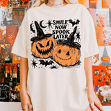 Smile Now Spook Later DTF Heat Transfer, Halloween-themed t-shirt featuring two orange pumpkins with witch hats, jack-o'-lantern faces, surrounded by bats, stars, and spooky text.
