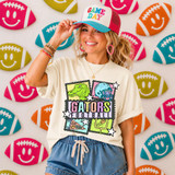 Retro Mascot Collage DTF Heat Transfer, vibrant and playful football-themed design featuring a dinosaur, football helmet, sports-related icons, and the text GATORS FOOTBALL, on a woman's white t-shirt in front of a backdrop with colorful smiley face footballs.